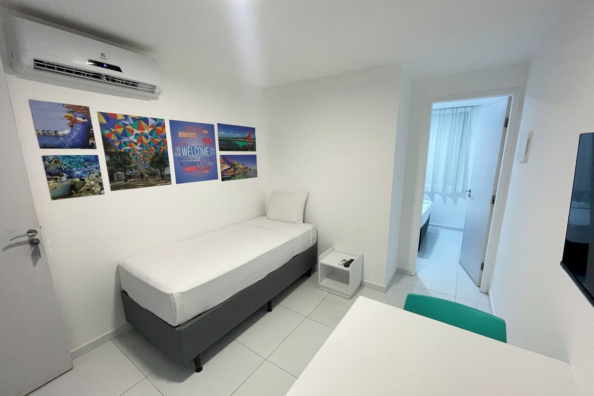 A bedroom with a bed, a small bedside table, and a wall with several posters.