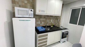 A compact kitchen with a microwave, sink, stove, and storage drawers. - Porto Sol Flats by AFT (Ipojuca)