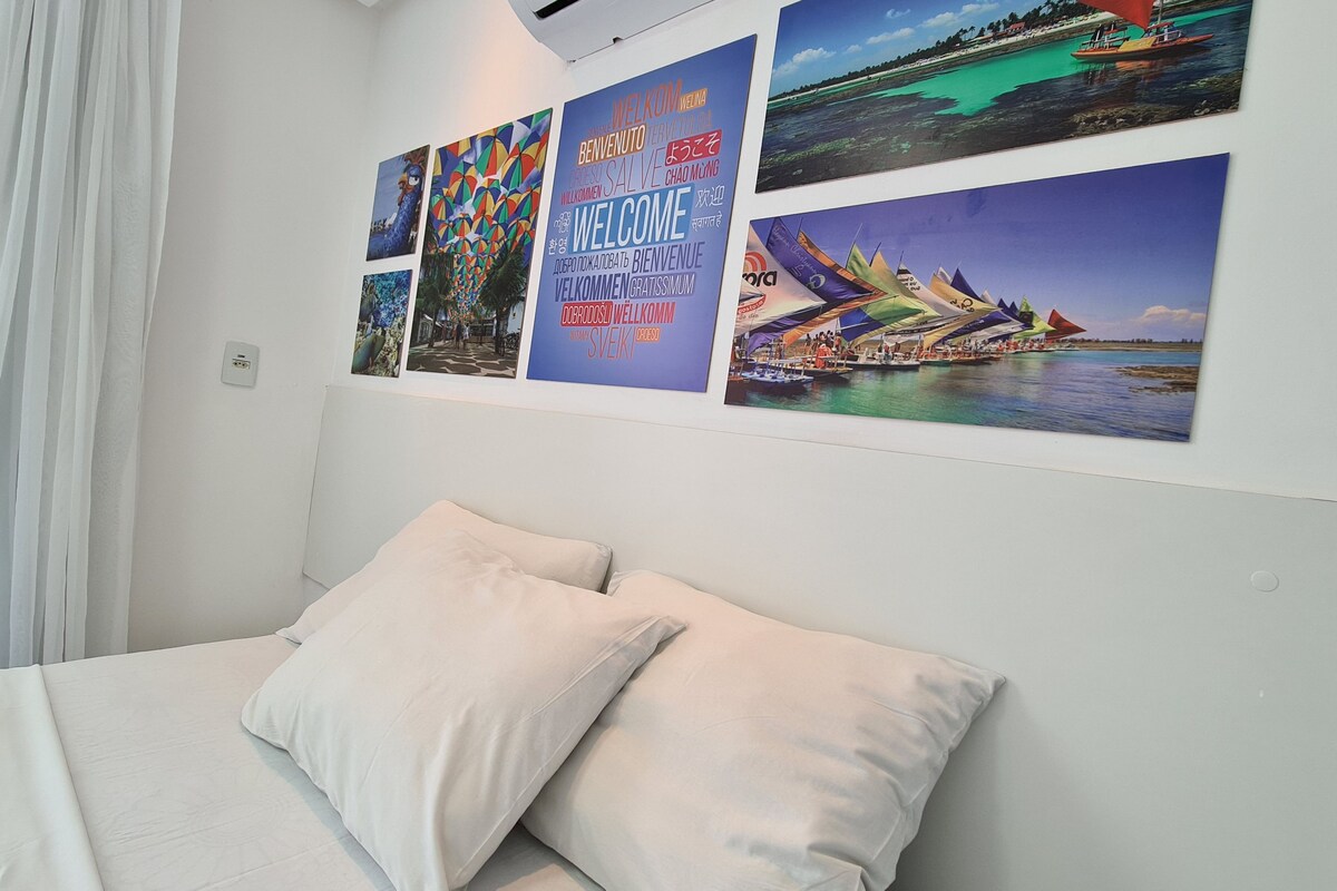 A bedroom with a bed, pillows, and a wall decorated with colorful welcome posters.