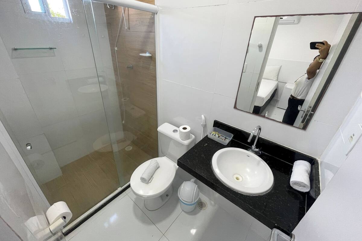Un baño moderno con ducha envuelta en vidrio, inodoro blanco, lavamanos con encimera negra y espejo.