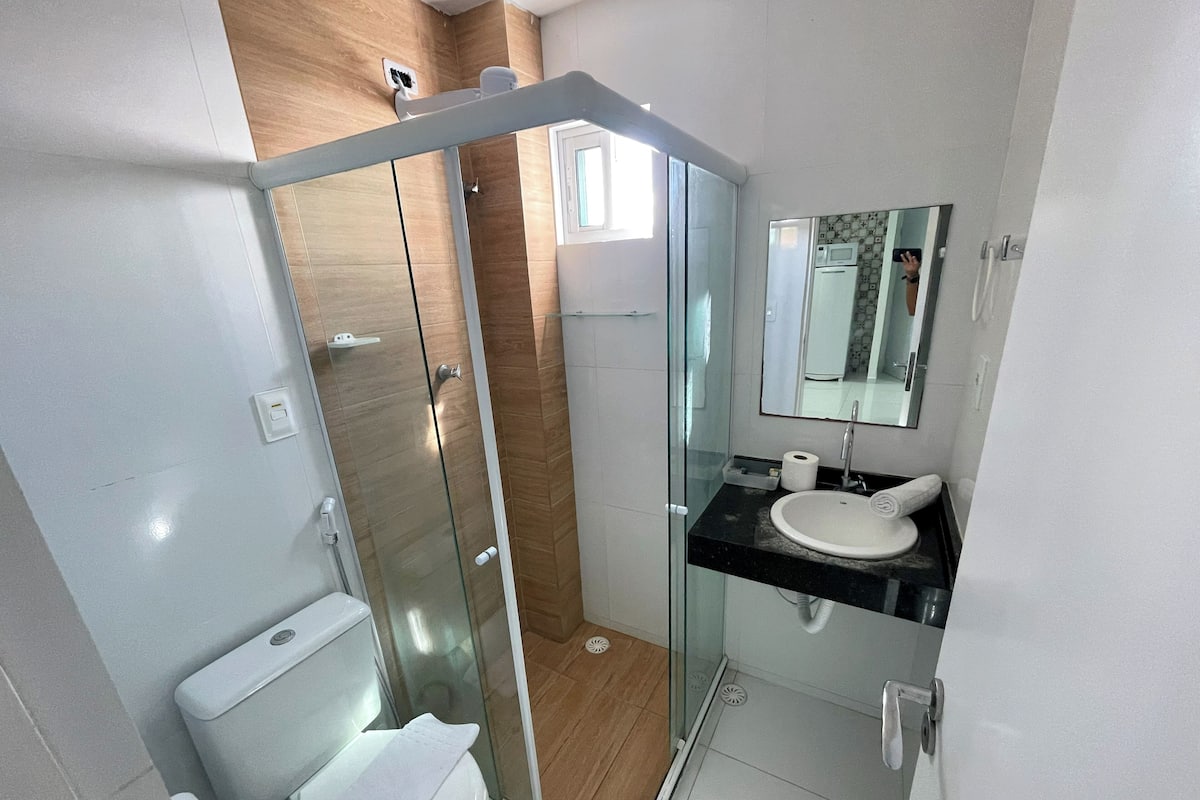 Un baño moderno con ducha de vidrio, inodoro blanco y lavamanos con espejo.