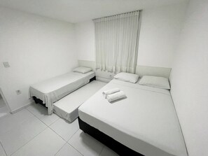 A room with two beds, a window with curtains, and a white tiled floor. - Porto Sol Flats by AFT (Ipojuca)