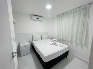Habitación de hotel con una cama, mesita de noche, un pequeño armario y una ventana con cortinas.