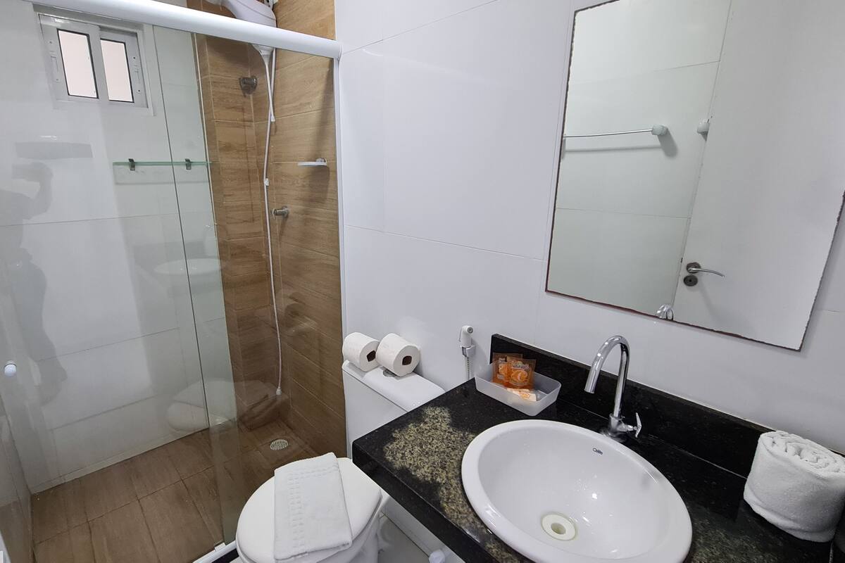Un baño con cabina de ducha de vidrio, lavabo blanco, espejo y retrete.