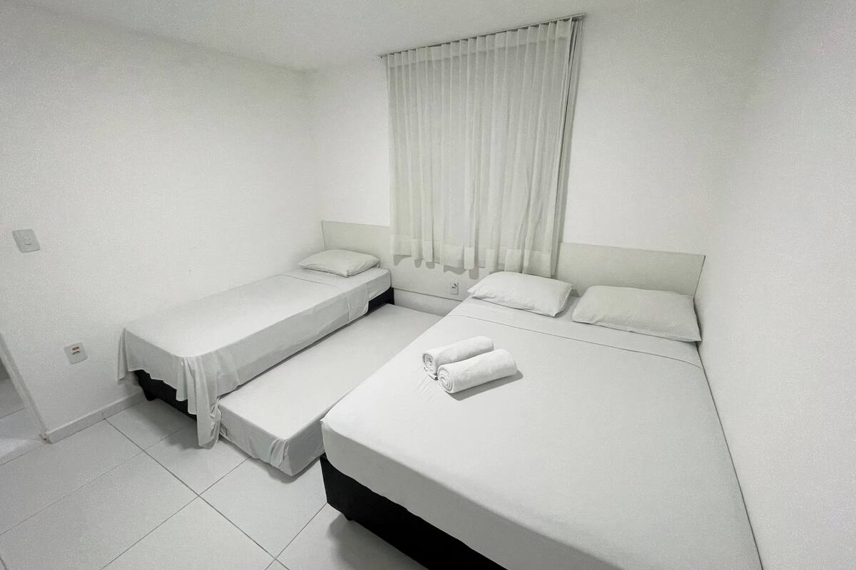 Una habitación con dos camas, una ventana con cortinas y un piso de baldosas blancas.