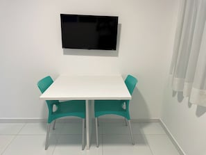 A small, white dining area with a single table and two teal chairs. A flat-screen TV is mounted on the wall above the table. - Porto Sol Flats by AFT (Ipojuca)
