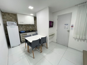 A compact kitchen with white cabinets, a microwave, and a refrigerator. There is a dining table with four chairs. - Porto Sol Flats by AFT (Ipojuca)