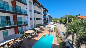 Un hotel de varios pisos con piscina, mobiliario exterior y balcones.
