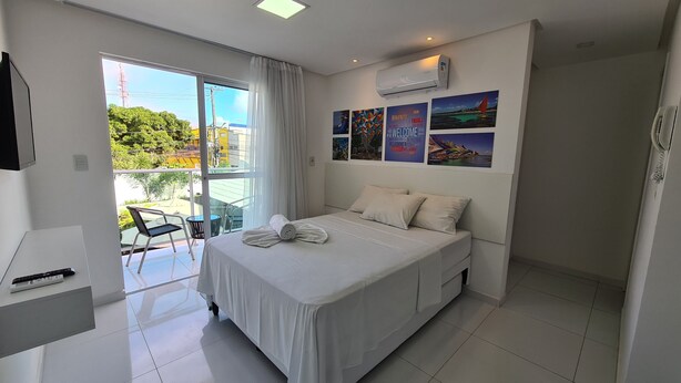 A hotel room with a bed, a desk, a chair, and a view of the outdoors. - Porto Sol Flats by AFT (Ipojuca)