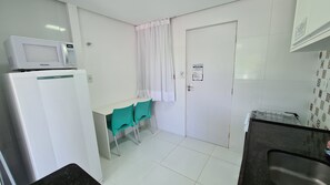A small, clean kitchenette with a microwave, a refrigerator, a sink, and a window with curtains. - Porto Sol Flats by AFT (Ipojuca)