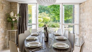 Comedor con una mesa dispuesta para seis comensales, ventanas amplias y una pared de piedra.