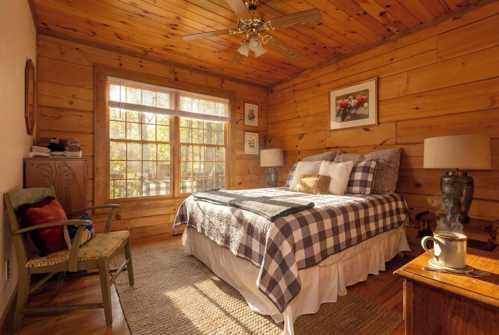 Un dormitorio de cabaña de madera con cama, una silla, una mesa con lámpara y una ventana.