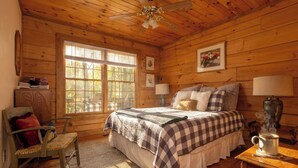 Une chambre dans une cabane en bois, avec un lit, une chaise, une table avec une lampe et une fenêtre.