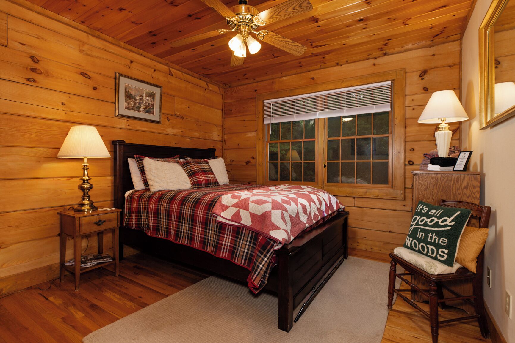 A wooden cabin bedroom with a bed, a nightstand, a chair, a window, and a ceiling fan.