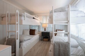 Ein Mehrbettzimmer mit Nachttisch, Lampe und Fenster mit Jalousien.