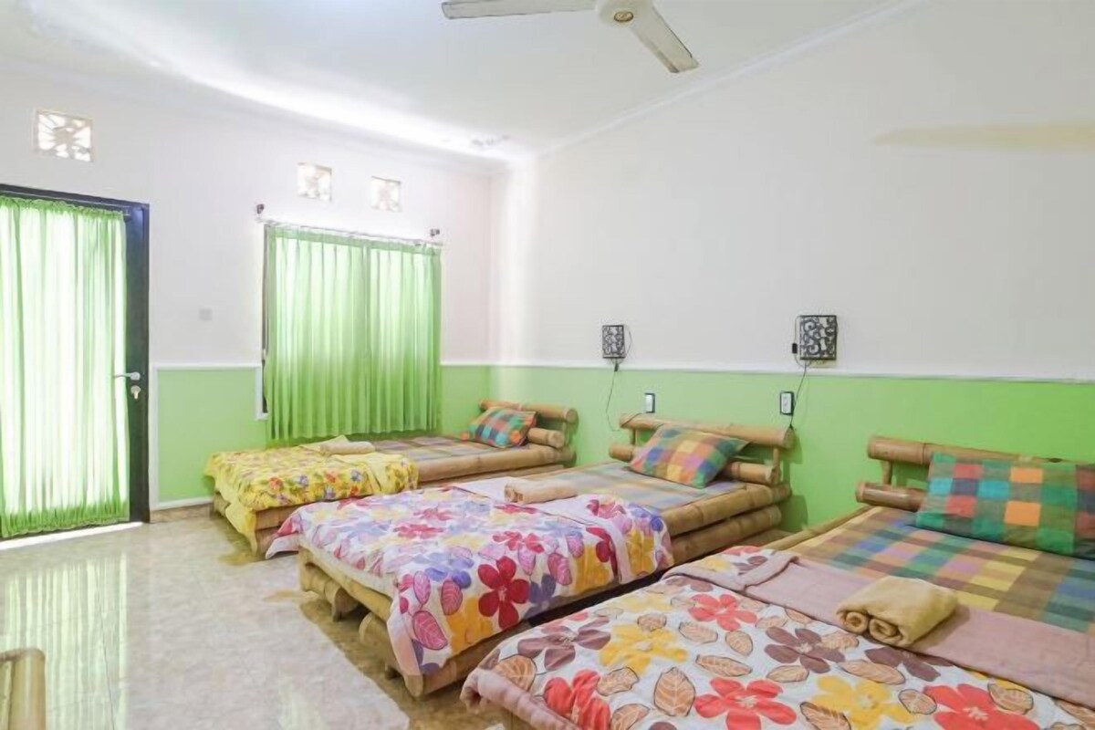 Ein Zimmer mit drei Betten, einer grünen Tür und einem Deckenventilator.