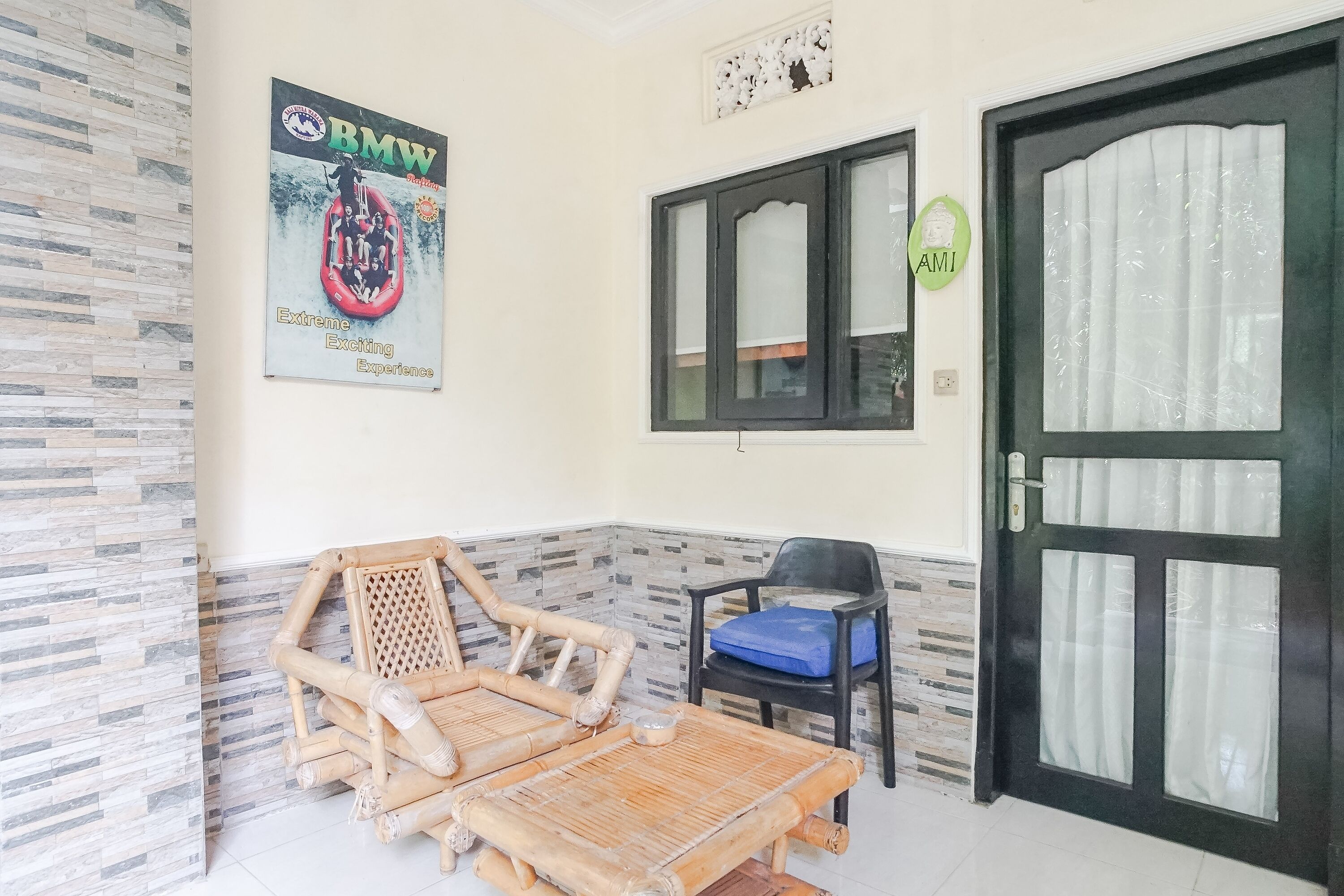 A room with a tiled floor, a poster of a BMW car, a black door with glass panels, and a bamboo chair.