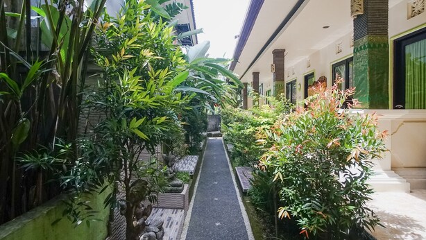 A narrow pathway flanked by lush greenery and a building with traditional architectural elements. - Green View Ubud Hostel Bali (Ubud)