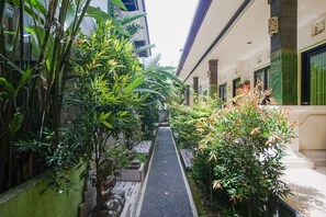 A narrow pathway flanked by lush greenery and a building with traditional architectural elements. - Green View Ubud Hostel Bali (Ubud)