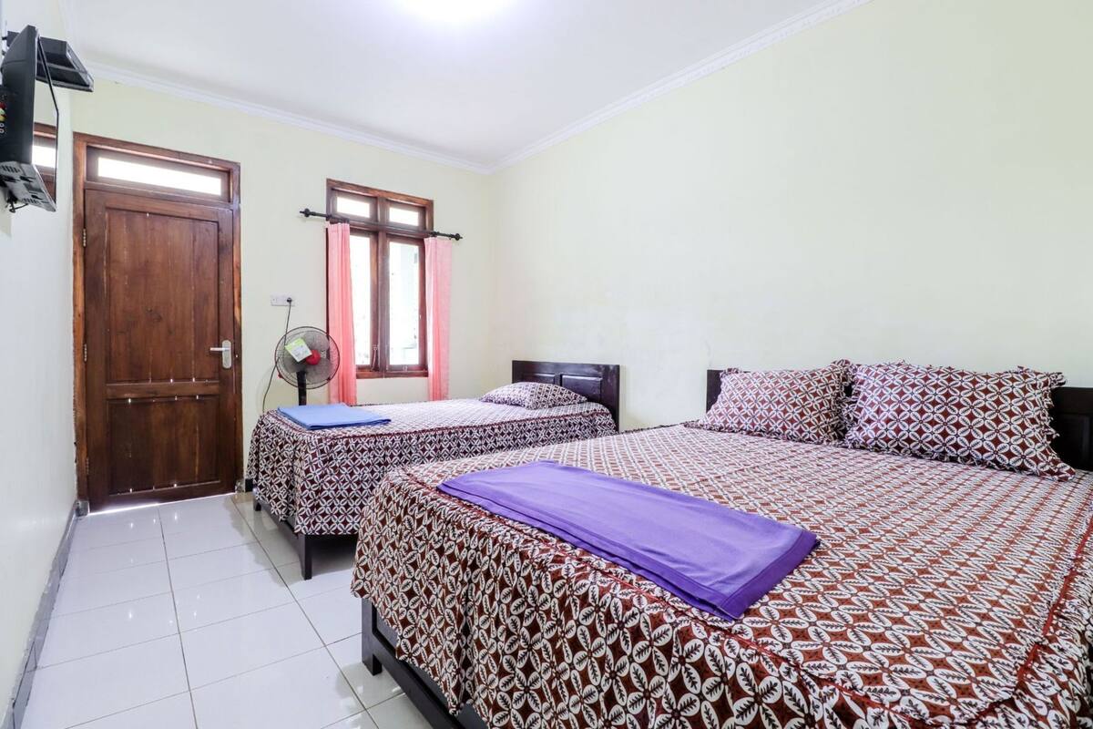 A room with two beds, a door, a window with curtains, and a fan.