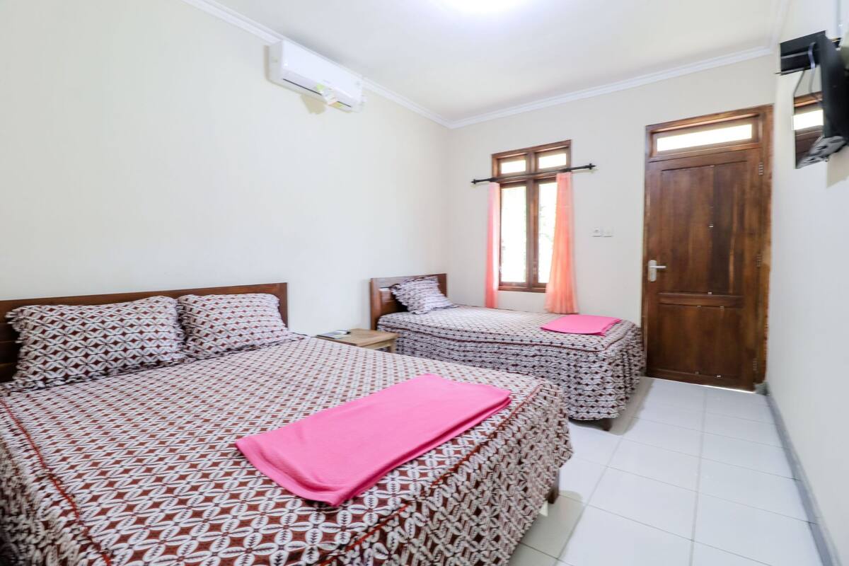 A bedroom with two beds, a wooden door, and a window with curtains.