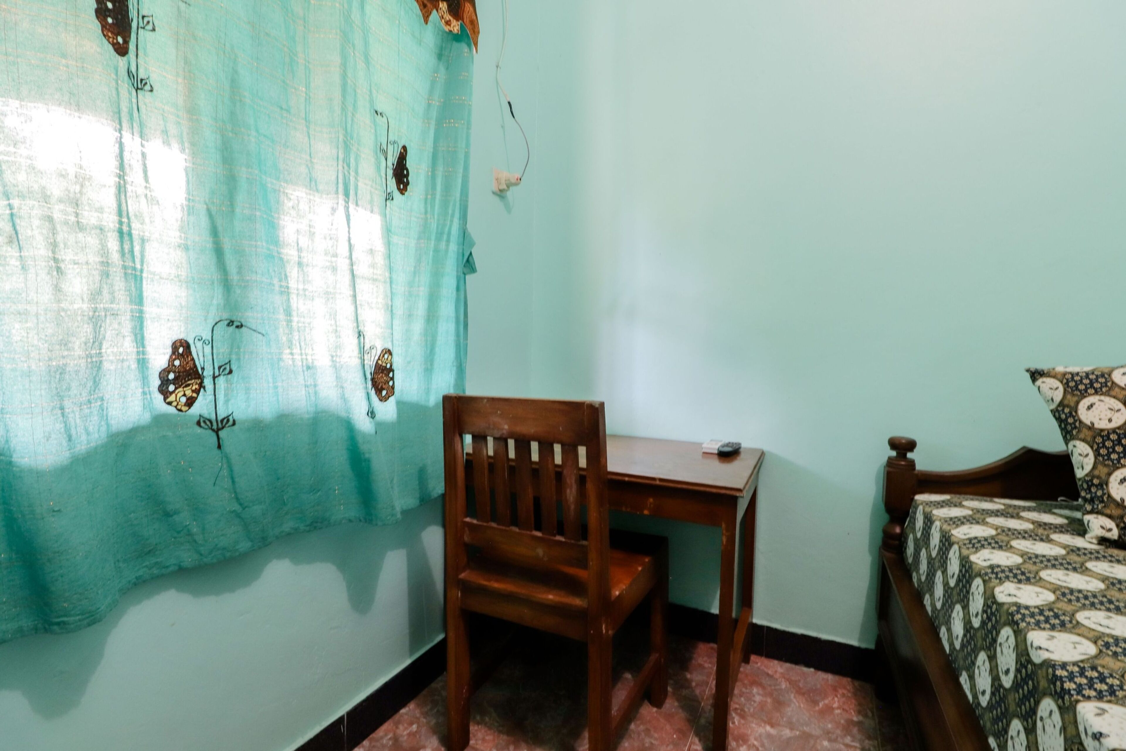 Una habitación con una silla de madera, una mesita pequeña, una cama con ropa de cama estampada y una cortina con diseños de mariposas.