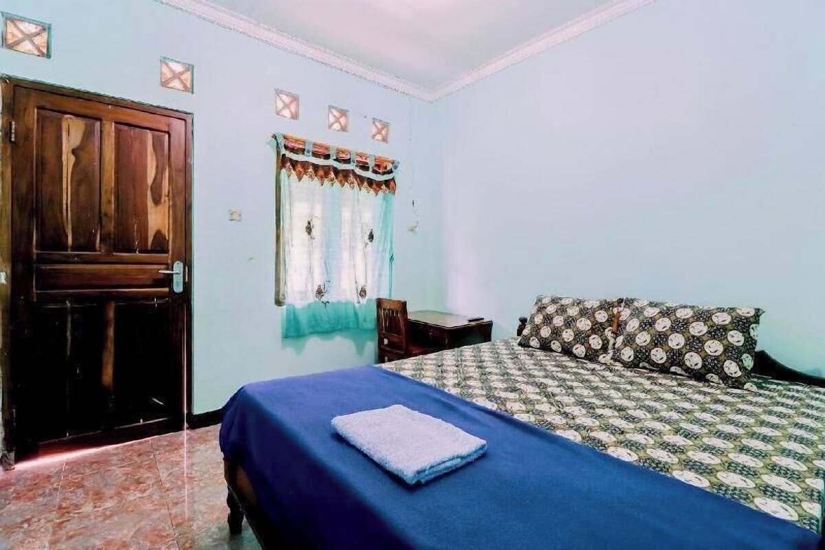 A bedroom with a bed, a wooden door, a window with curtains, and a patterned pillow.