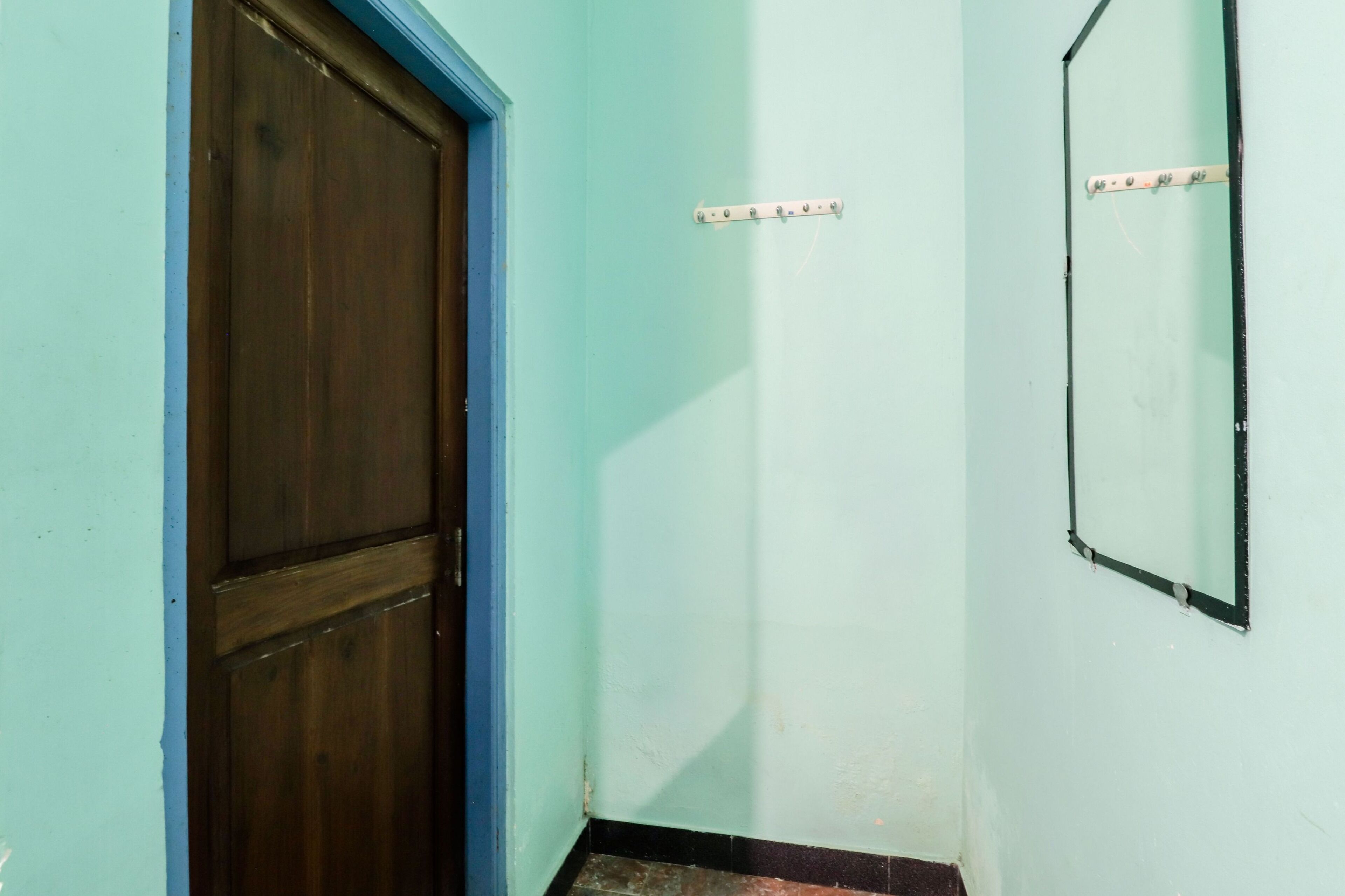 A narrow hallway with a wooden door and a wall-mounted mirror.