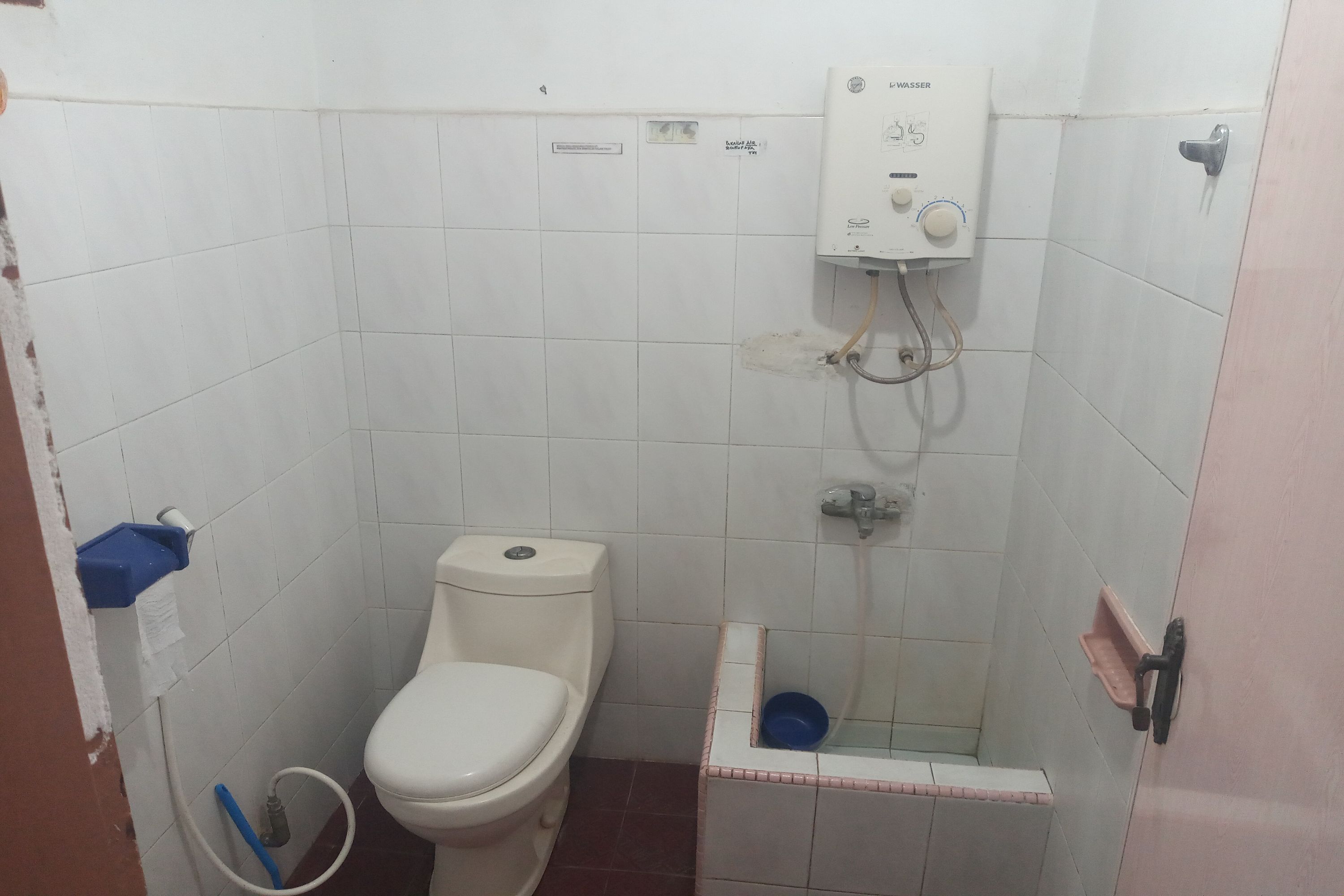A small, tiled bathroom with a toilet, a shower, and a blue basin.