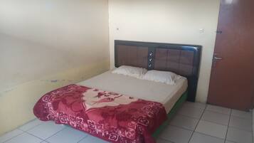 Una cama individual con una colcha estampada, cabecera de madera y una puerta a la derecha.
