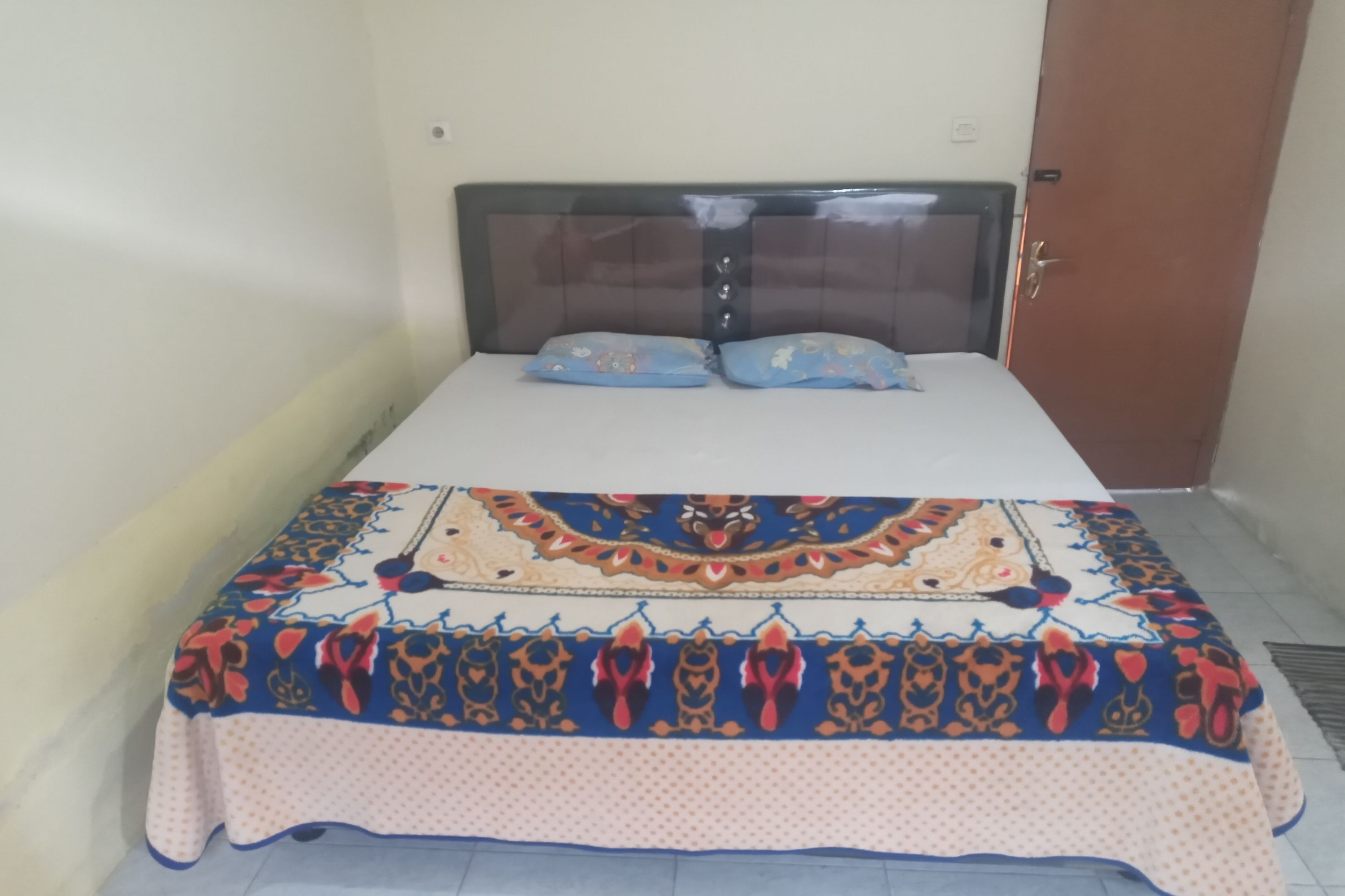 A bed with a patterned bedspread and two pillows, a wooden headboard, and a door to the right.