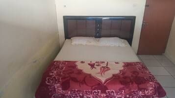 Una cama pequeña y bien hecha con una colcha estampada y almohadas, un cabecero de madera y una puerta cerrada a la derecha.