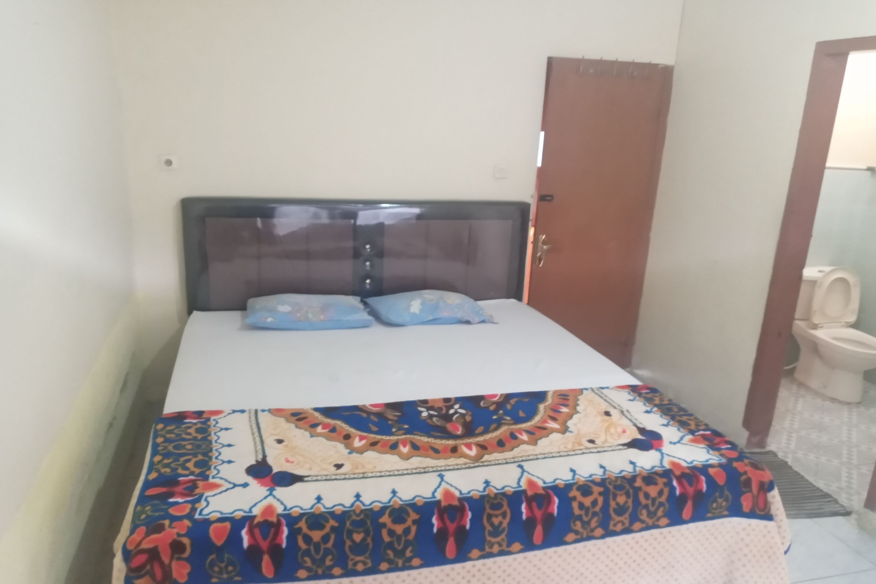 A bedroom with a bed, two pillows, a wooden headboard, and a bathroom with a toilet and sink.