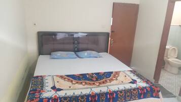 A bedroom with a bed, two pillows, a wooden headboard, and a bathroom with a toilet and sink.