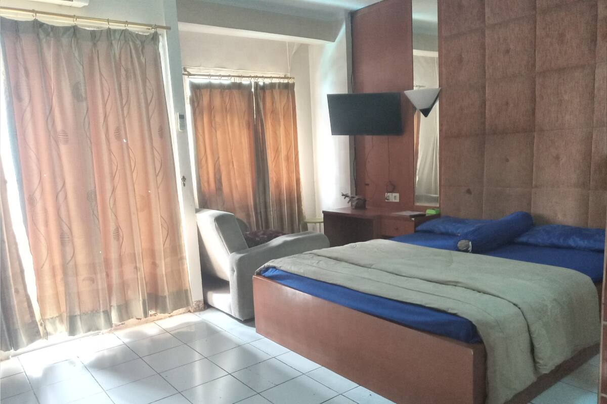 Een hotelkamer met een bed, een bureau, een stoel, een televisie en een raam met gordijnen.