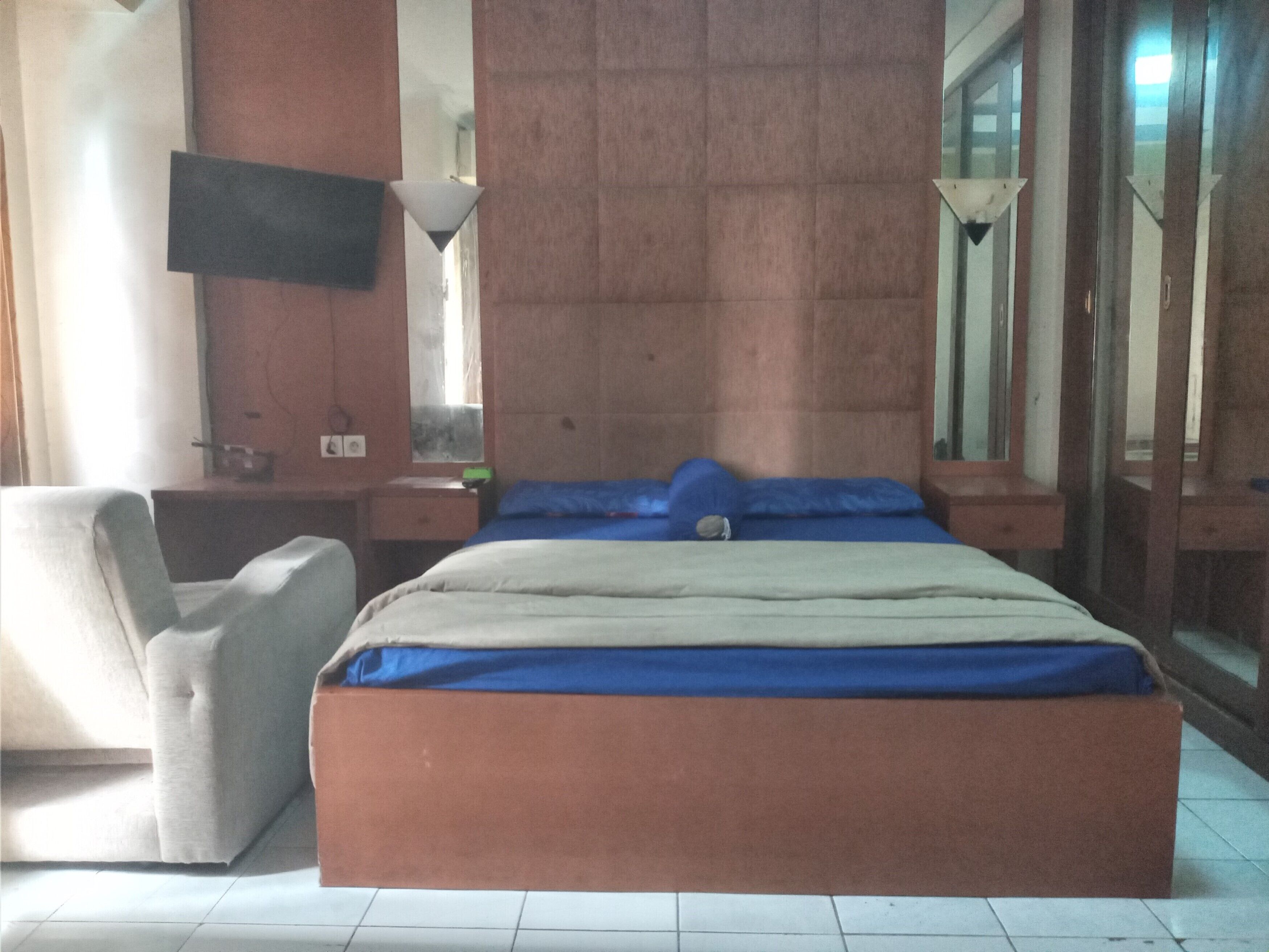 A bedroom with a bed, a chair, a desk, a mirror, and a television.