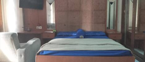 A bedroom with a bed, a chair, a desk, a mirror, and a television.