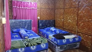 Una habitación con dos camas, cada una con ropa de cama del Chelsea Football Club. La habitación tiene paredes de madera y una cortina rosa.
