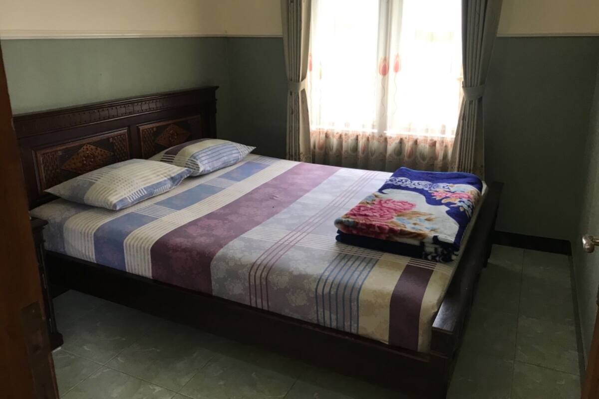 Una cama individual con cabecera de madera, colcha a rayas y una manta estampada doblada al pie.
