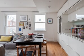 A modern kitchen with white cabinetry, a dining table set for four, and a bookshelf filled with books.