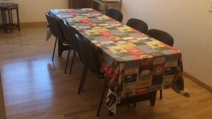 Een eethoek met een lange tafel, bedekt met een kleurrijke tafelkleed, omringd door stoelen.