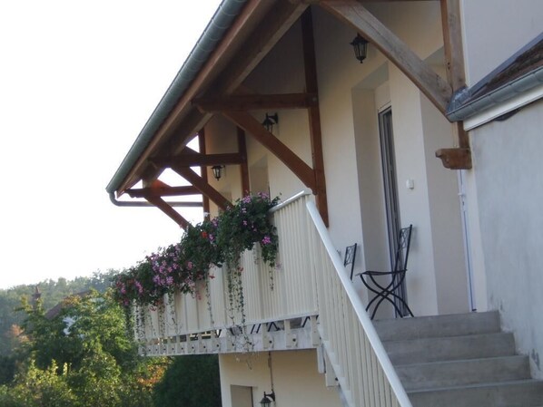 Un balcon avec des balustrades en bois et des jardinières, un escalier et une vue sur une zone boisée.