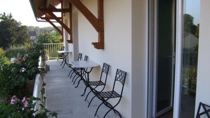 Een terras buiten met een tafel en stoelen, een houten pergola en een schuifdeur die leidt naar een balkon.