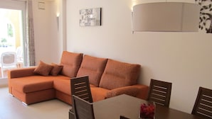 A modern living room with a sectional sofa, a dining table with chairs, and a decorative piece on the wall. - APARTMENT-COMMUNITY POOL-CUMBRE DEL SOL-CLOSE TO MORAIRA-BEAUTIFUL VIEWS (BENITACHELL)