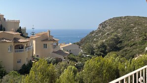 A coastal town with Mediterranean-style buildings, a clear view of the sea, and a hillside with dense vegetation. - APARTMENT-COMMUNITY POOL-CUMBRE DEL SOL-CLOSE TO MORAIRA-BEAUTIFUL VIEWS (BENITACHELL)