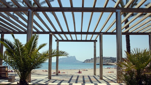 A beach view with a wooden pergola, palm trees, and a clear sky. - APARTMENT-COMMUNITY POOL-CUMBRE DEL SOL-CLOSE TO MORAIRA-BEAUTIFUL VIEWS (BENITACHELL)