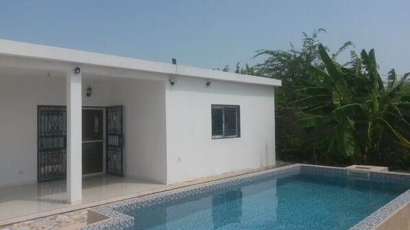 A modern house with a swimming pool, a covered patio, and a large window.