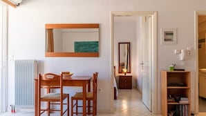 Une petite pièce bien éclairée, avec une table et des chaises en bois, un miroir, un radiateur et une bibliothèque.