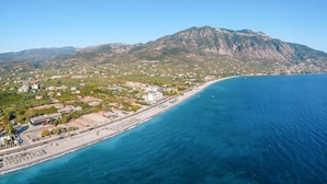 Une vue aérienne d’une ville côtière, avec une montagne en arrière-plan, une plage et une route qui longe la côte.