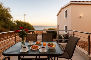 Un balcón con una mesa dispuesta para el desayuno, que incluye croissants, fruta y café.